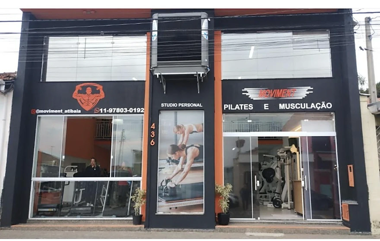 Fachada preta e laranja do Moviment Studio com vitrines de pilates e musculação